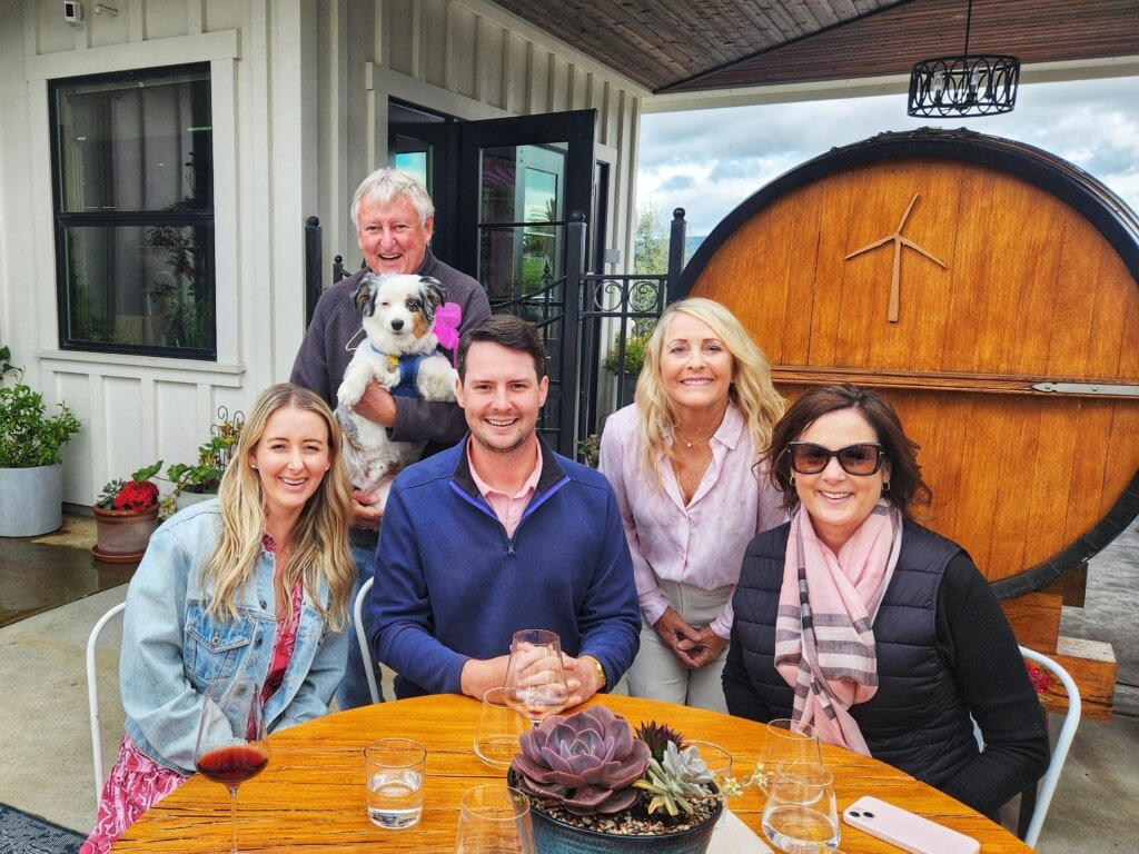 Group of guests and dog wearing pink at Winery with big wine cask in backgroun